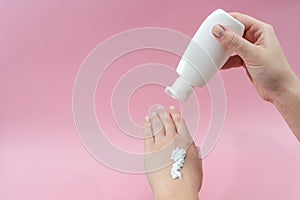 Female hands squeezing cream from tube on pink background. Ð¡osmetic bottles for beauty or medicine products