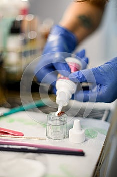 Female hands squeezing paint into a glass cup for mixing eyebrow paint