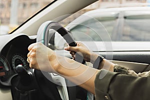 Female hands on the steering wheel of a car while driving on the road.