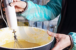 Female hands stirring dough with a mixer for cake or bread in a bowl on a kitchen worktop, preparation for baking.