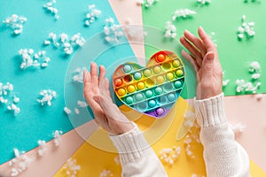 Female hands surround a silicone rainbow antistress toy in the shape of a heart on a cardboard of different colors and fluff.