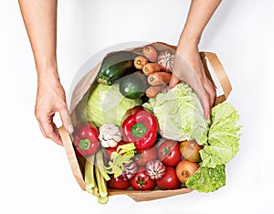 Female hands take a head of Chinese cabbage from a paper bag with various vegetables  on a white background. Delivery and