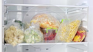Female Hands take out bags of frozen vegetables in the fridge. Frozen fruits, vegetables, meat in the freezer.