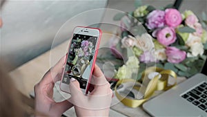 Female hands taking photo of beautiful flowers with smartphone in flower shop, florist with phone and laptop
