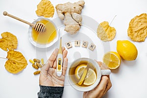 Female hands with tea and thermometer, lemon, ginger, honey, tab