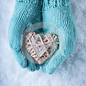 Female hands in teal knitted mittens with a entwined vintage romantic heart on a snow background. Love and St. Valentine concept