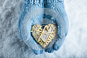 Female hands in teal knitted mittens with a entwined vintage romantic heart on a snow background. Love and St. Valentine concept