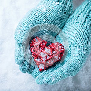 Female hands in teal knitted mittens with a entwined vintage romantic heart on a snow background. Love and St. Valentine concept