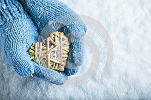 Female hands in teal knitted mittens with a entwined vintage romantic heart on a snow background. Love and St. Valentine concept