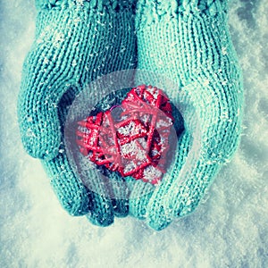 Female hands in teal knitted mittens with a entwined vintage romantic heart on a snow. Love and St. Valentine concept.