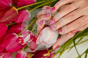 Female hands with tender spring manicure holding pink fresh tulip on flowers background. Nail art, gel nails polish design