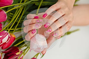 Female hands with tender spring manicure holding pink fresh tulip on flowers background. Nail art, gel nails polish design and bea