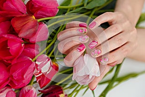 Female hands with tender spring manicure holding pink fresh tulip on flowers background. Nail art, gel nails polish design, beauty