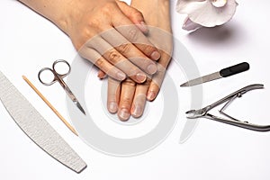 Female hands and tools for edged manicure nail file, cuticle nippers, scissors, orange stick.