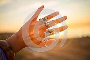 Female hands touch the sun. Hippie woman hands with silver rings at sunset. Indie boho vibes and bohemian style
