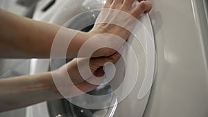 Female hands trys to open laundry machine and takes White CLOTHES. Loading washing machine. Load clothes to washer