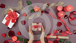 Female hands are tying red ribbon bow on wrapped gift box for St. Valentine`s Day. Woman is preparing present gift for 14th of Feb