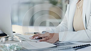 Female hands typing an email on her computer keyboard with her sitting her office desk. Close up of a professional