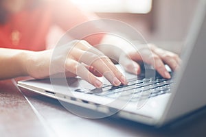 Female hands typing on keyboard of laptop surfing Internet and texting friends via social networks, sitting at wooden table indoor