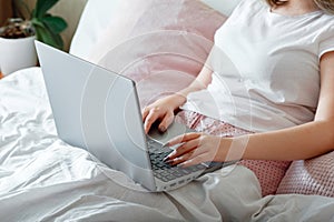 Female hands typing on laptop keyboard while lying in bed. Woman work using laptop while sitting in bed at morning home. Teen girl