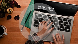 Female hands typing on laptop keyboard on wooden table with flower vase