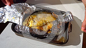 Female hands unfolding of baked fish in foil