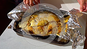 Female hands unfolding of baked fish in foil