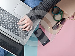 Female hands use a laptop on the background of a bag, smartphone, smart bracelet and other gadgets and accessories. Top view