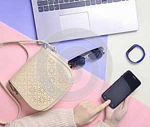 Female hands use a smartphone on the background of a bag, laptop.