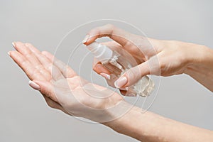 Female hands using hand sanitizer spray dispenser over light grey background