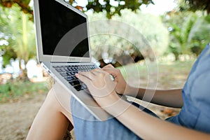 Female hands using laptop with sand in background, black screen.