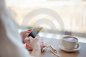 Female hands using mobile phone for organising schedule while drinking latte during the coffee break