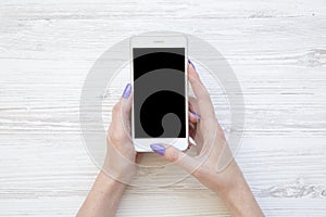 Female hands using smartphone on white wooden background, top view.
