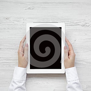 Female hands using tablet over white wooden surface, top view. From above, overhead, flat lay