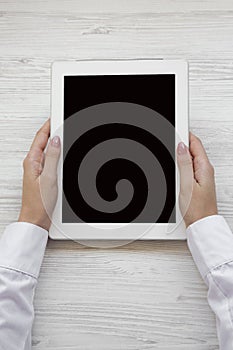 Female hands using tablet on a white wooden surface, top view. From above, overhead