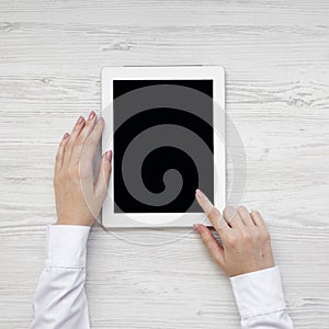 Female hands using tablet on a white wooden surface, top view. From above, overhead, flat lay