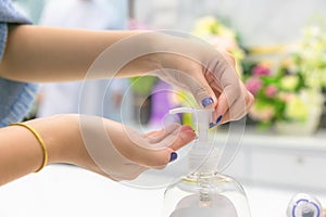 Female hands using wash hand sanitizer gel pump dispenser in clinic room