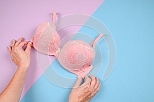 Female hands on a violetand blue background holding a beautiful pink bra. Daily underwear concept. Sales concept