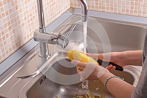 Female hands washing a peeling potato with hand under running water in sink in the kitchen