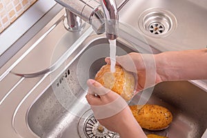 Female hands washing potato with hand under running water in sink in the kitchen