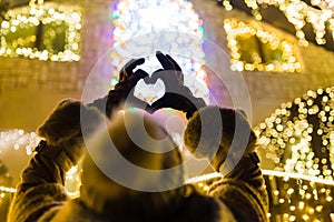 Female hands wearing gloves showing heart shape. Bokeh christmas new year decoration in the background