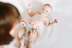 Female hands wearing pants for baby, a little kid lying on the bed nanny change diaper after bath, mother and baby