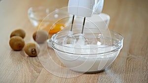 Female hands whipping egg whites cream in glass bowl with mixer.