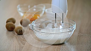 Female hands whipping egg whites cream in glass bowl with mixer.