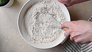 Female hands whisking flour dough batter in a bowl for pancakes or cake.