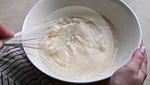 Female hands whisking flour dough batter in a bowl for pancakes or cake.
