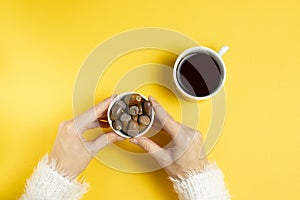 Female hands in a white fluffy sweater hold a plate with ripe acorns next to a mug with an alternative decaf coffee drink on a