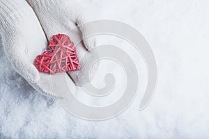 Female hands in white knitted mittens with entwined vintage romantic red heart on snow background. Love and St. Valentine concept