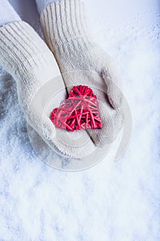 Female hands in white knitted mittens with entwined vintage romantic red heart on snow background. Love and St. Valentine concept