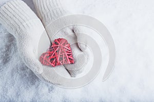 Female hands in white knitted mittens with entwined vintage romantic red heart on snow background. Love and St. Valentine concept